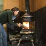 Woman putting firewood into wood stove